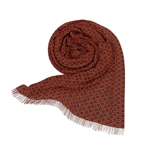 May include: A rolled-up scarf with a geometric pattern in shades of brown and red. The scarf has a fringed edge and a repeating hexagonal design. The scarf is made of a soft material.
