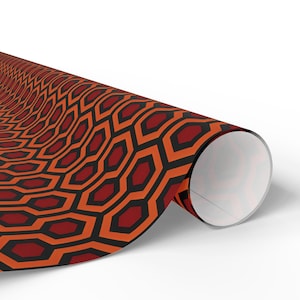 May include: A roll of patterned paper featuring a repeating geometric design. The pattern consists of black outlines around orange and maroon shapes, creating a honeycomb or hexagonal motif. The paper is rolled up, revealing the pattern.