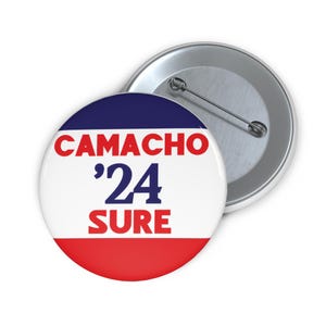 May include: A white, blue, and red button with the text "CAMACHO '24 SURE" in red and blue lettering.