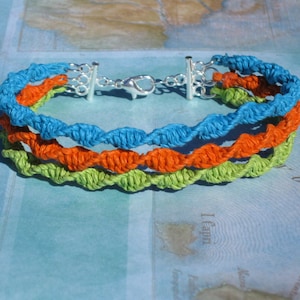 Op de afbeelding: Een meerstrengs armband gemaakt van geweven macramé koord in tinten groen, oranje en blauw. De armband heeft een zilveren sluiting.