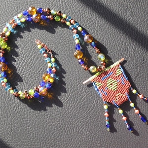 May include: A multi-strand necklace with green, blue, and brown beads. The necklace has a pendant with a woven design in red, green, and blue.