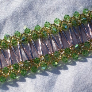 May include: A close-up of a green and gold beaded bracelet with silver-toned spacers. The bracelet is made with small, faceted beads and is arranged in a repeating pattern.