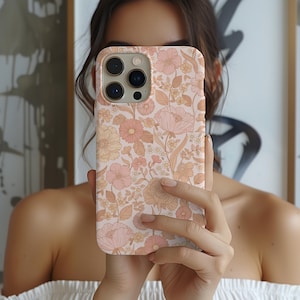 Puede incluir: Una funda de teléfono rosa y marrón con estampado floral y un recorte para el objetivo de la cámara. La funda tiene un estampado floral vintage.