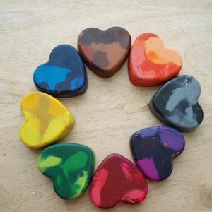 Puede incluir: Una colecci&oacute;n de ceras en forma de coraz&oacute;n en varios colores, incluyendo azul, marr&oacute;n, naranja, gris, morado, rojo, verde y amarillo. Las ceras est&aacute;n dispuestas en un patr&oacute;n circular sobre una superficie de madera clara.