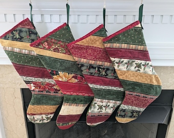 Puede incluir: Cuatro calcetines navideños con rayas de tela verdes, rojas y doradas. Cada calcetín presenta un patrón diferente, incluyendo diseños florales y a cuadros. Cintas verdes cuelgan los calcetines de una repisa blanca.