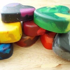Puede incluir: Una colecci&oacute;n de ceras en forma de coraz&oacute;n en varios colores, incluyendo amarillo, azul, verde, rojo y negro. Las ceras est&aacute;n apiladas, mostrando sus tonos y texturas mixtas. La imagen est&aacute; bien iluminada, resaltando los colores vibrantes de los materiales de arte.