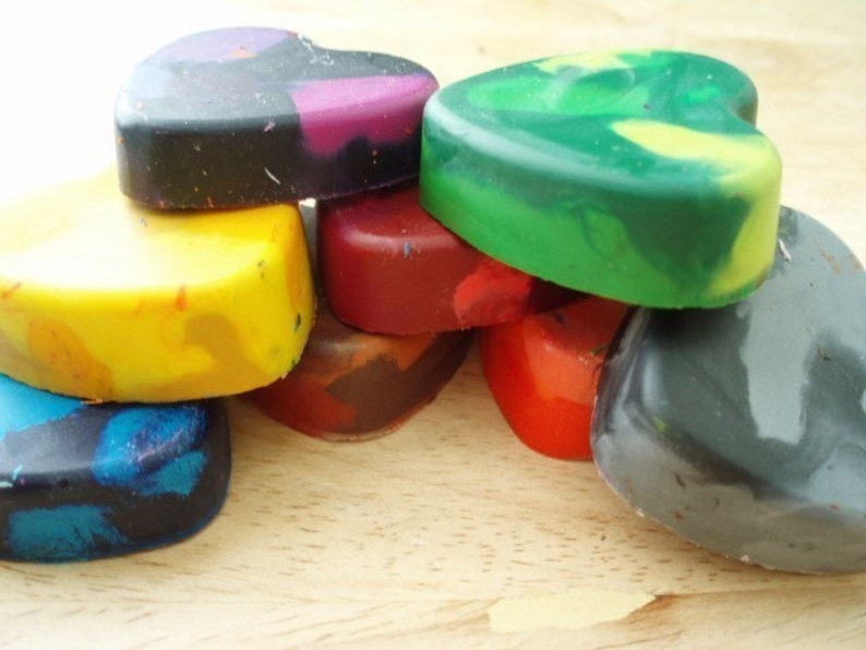 Puede incluir: Una colecci&oacute;n de ceras en forma de coraz&oacute;n en varios colores, incluyendo amarillo, azul, verde, rojo y negro. Las ceras est&aacute;n apiladas, mostrando sus tonos y texturas mixtas. La imagen est&aacute; bien iluminada, resaltando los colores vibrantes de los materiales de arte.