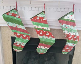 Puede incluir: Tres calcetines navideños colgados sobre una chimenea. Cada calcetín está hecho de tiras de tela rojas, verdes y blancas, con motivos de Papá Noel y festivos. Los calcetines tienen lazos rojos para colgar y ribetes verdes.