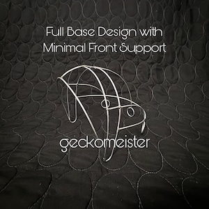 May include: A silver wireframe hat form with a full base design and minimal front support. The text "Full Base Design with Minimal Front Support" and "geckomeister" are displayed in white. The background is a black quilted fabric.