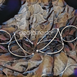 May include: Two silver-toned metal hoops with a curved design, resting on a patterned fabric background. The text "geckomeister" is visible in the center of the image.