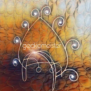 May include: A silver wire sculpture of a peacock with its tail feathers spread out. The sculpture is on a brown quilted background.