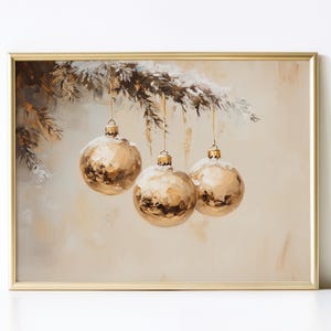 May include: A framed painting depicts three gold Christmas ornaments hanging from a snow-covered evergreen branch. The ornaments have a textured, metallic finish, and the background is a soft, neutral color.