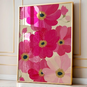 May include: A framed floral art print featuring large, vibrant pink flowers with yellow centers against a light beige background. The artwork is enclosed in a gold frame, creating a striking contrast. The flowers are painted in varying shades of pink.