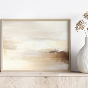 May include: Abstract landscape painting in a light beige wooden frame. The artwork features a blend of beige, cream, and brown brushstrokes, creating a serene and minimalist aesthetic. A white vase with dried flowers is on the right.