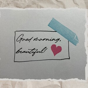 May include: A light blue note with a piece of blue tape on the top. The note says "Good morning, beautiful!" with a pink heart drawn next to the text.