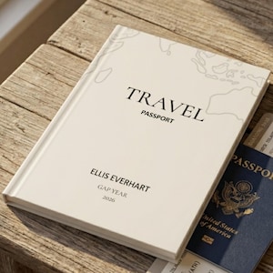 May include: A cream-coloured travel journal with the words "TRAVEL PASSPORT" on the cover. The journal also includes the name "ELLIS EVERHART" and "GAP YEAR 2026". A U.S. passport is visible.