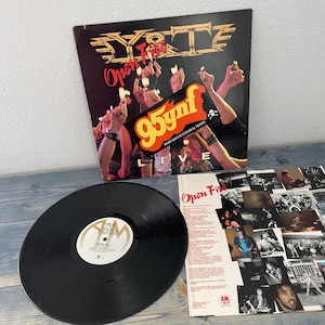 May include: A black vinyl record and album cover for the band D.Y.T.E. The album cover is black with gold lettering and features the text "Open Fire Live". A sticker on the cover reads "95ynf Tampa Bay's Rock N Roll Faves".