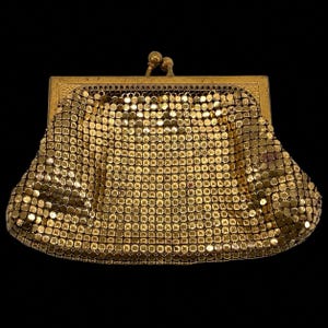 May include: A vintage gold mesh purse with a rectangular frame and a kiss-lock clasp. The purse is made of small, circular metal pieces, creating a shimmering effect. The frame and clasp are also gold-toned.