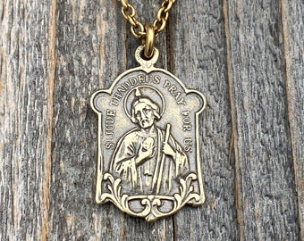 Op de afbeelding: Een messingkleurige metalen hanger aan een ketting met een rechthoekige religieuze medaille met een reliëf van de heilige Judas Thaddeus die een staf en een klein voorwerp vasthoudt. De tekst ST JUDE THADDEUS PRAY FOR US staat op de rand.