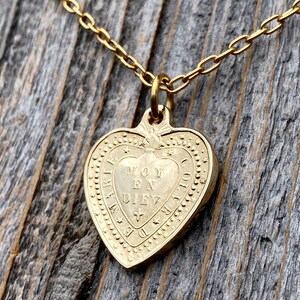 May include: Gold heart-shaped pendant necklace with a delicate chain. The pendant features an inscription that reads "Moy En Diev", surrounded by a decorative border.