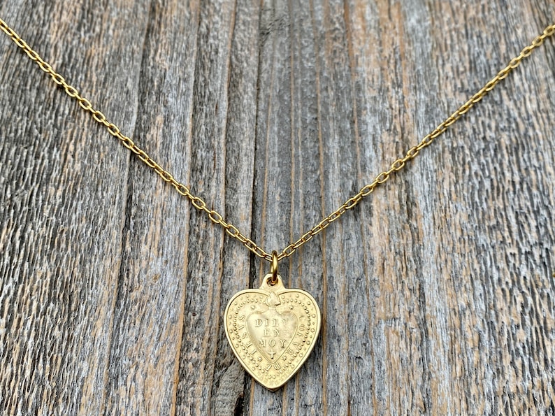 May include: Gold heart-shaped pendant necklace with the inscription "DIV IN NOY" on a gold chain.