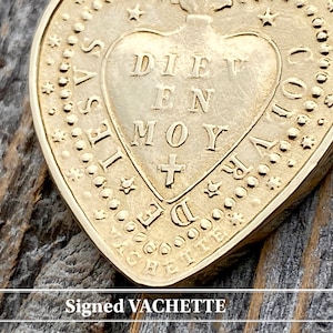 May include: A gold heart-shaped pendant with the inscription "DIEU EN MOY" and a cross inside the heart. The pendant is surrounded by a border of stars and dots. The pendant is signed "VACHETTE".