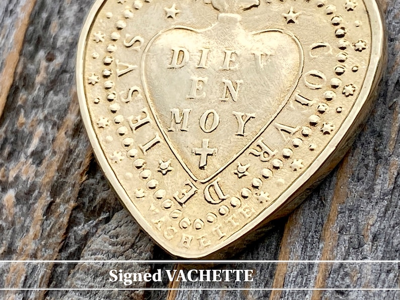 May include: A gold heart-shaped pendant with the inscription "DIEU EN MOY" and a cross inside the heart. The pendant is surrounded by a border of stars and dots. The pendant is signed "VACHETTE".