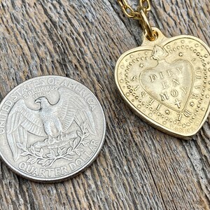 May include: A gold heart-shaped pendant necklace with a chain. The pendant has the words "DIEV EN MOY" inscribed on it.