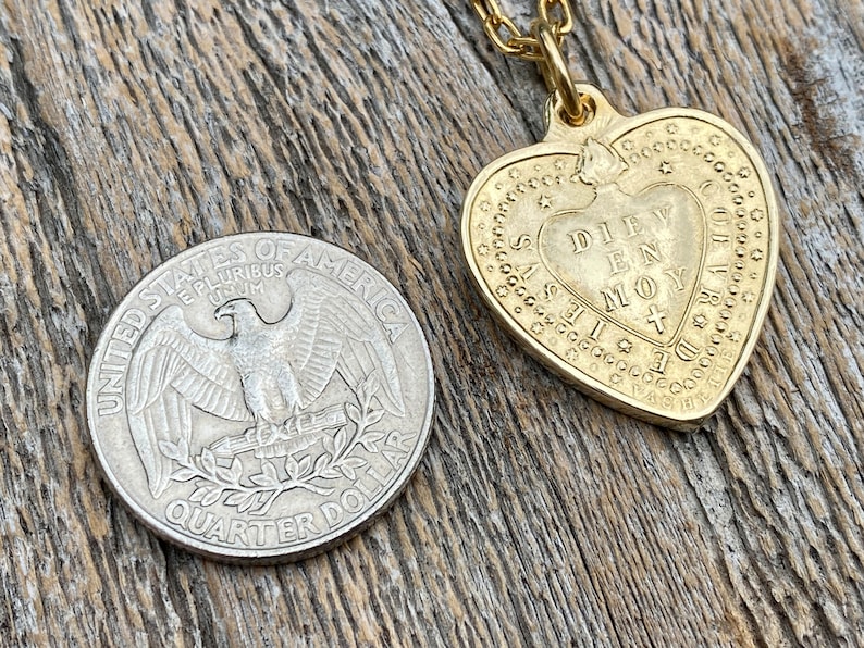 May include: A gold heart-shaped pendant necklace with a chain. The pendant has the words "DIEV EN MOY" inscribed on it.