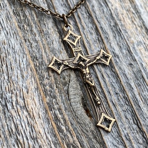 Crucifijo barroco de bronce, réplica antigua, procedente de la Santa Sede de Roma. Collar con colgante de crucifijo. Cruz de bronce grande con extremos abiertos de trébol.