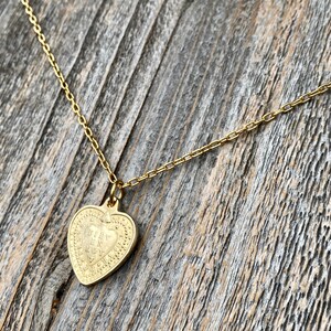 May include: A gold chain necklace with a heart-shaped pendant. The pendant has a detailed design with a heart inside.