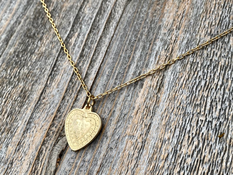 May include: A gold chain necklace with a heart-shaped pendant. The pendant has a detailed design with a heart inside.