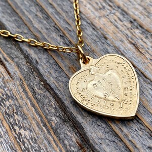 May include: Gold heart-shaped pendant necklace with a delicate chain. The pendant features an inscription that reads "DILLY DALLY IN MY MOY".