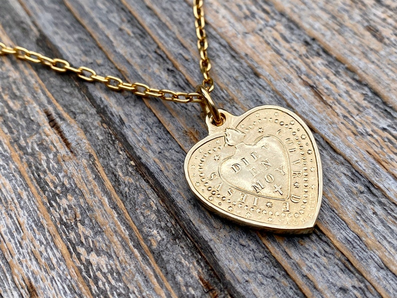 May include: Gold heart-shaped pendant necklace with a delicate chain. The pendant features an inscription that reads "DILLY DALLY IN MY MOY".