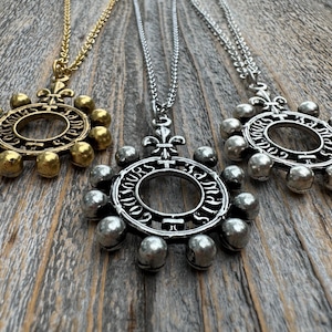 Peut inclure: Trois colliers en argent et en or avec un pendentif circulaire orné d'un motif de fleur de lys et d'une rangée de petites cloches. Le pendentif porte l'inscription "TOUS JOURS" autour de l'anneau.