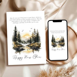 Könnte beinhalten: Eine Grußkarte und ein Smartphone zeigen eine Aquarelllandschaft mit Kiefern, einem Fluss und einem Sonnenuntergang. Auf der Karte und dem Telefon steht "Happy New Year" und eine Botschaft über Frieden und Freude.