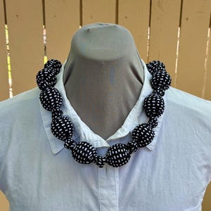 Puede incluir: Un collar de tela con lunares negros y blancos con cuentas grandes y redondas.