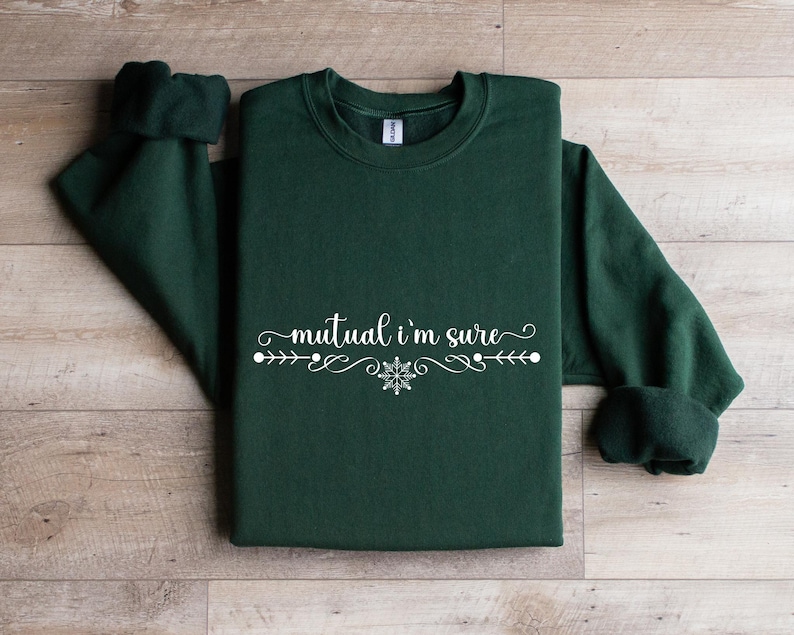 Puede incluir: Una sudadera de cuello redondo en color verde bosque oscuro con el texto blanco "mutual i'm sure" en una fuente cursiva, centrado sobre un elemento decorativo de l&iacute;nea con un peque&ntilde;o icono de copo de nieve en el centro.
