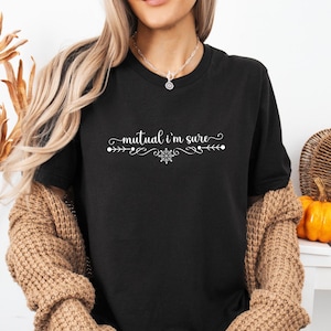 Puede incluir: Una camiseta negra de manga corta con el texto blanco "mutual i'm sure" en letra cursiva. El texto est&aacute; centrado y decorado con adornos sim&eacute;tricos y un peque&ntilde;o icono de copo de nieve situado justo debajo de las letras.
