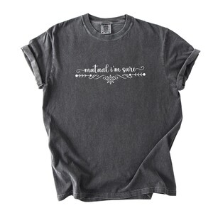 Puede incluir: Una camiseta de manga corta en color gris carb&oacute;n con el texto blanco "mutual i'm sure" impreso en el pecho. El texto est&aacute; centrado y flanqueado por adornos blancos decorativos y un peque&ntilde;o icono en forma de estrella, creando un dise&ntilde;o equilibrado.