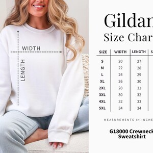 Puede incluir: Una sudadera blanca de cuello redondo junto a una tabla de tallas Gildan que muestra medidas de ancho, largo y manga en pulgadas para tallas de la S a la 5XL. La tabla incluye columnas para talla, ancho, largo y manga con valores num&eacute;ricos espec&iacute;ficos.