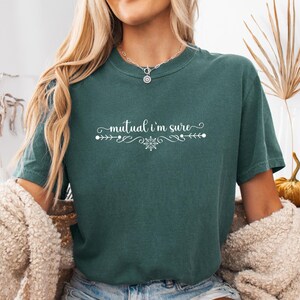 Puede incluir: Una camiseta de manga corta en color verde bosque oscuro con el texto blanco "mutual i'm sure" centrado en el pecho. El texto est&aacute; flanqueado por adornos blancos decorativos y un peque&ntilde;o icono de copo de nieve bajo la palabra "i'm".