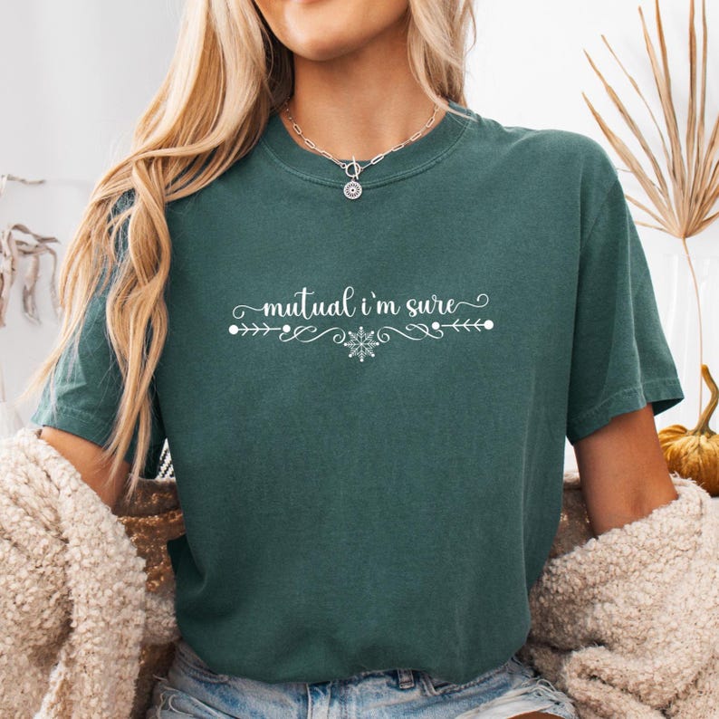 Puede incluir: Una camiseta de manga corta en color verde bosque oscuro con el texto blanco "mutual i'm sure" centrado en el pecho. El texto est&aacute; flanqueado por adornos blancos decorativos y un peque&ntilde;o icono de copo de nieve bajo la palabra "i'm".