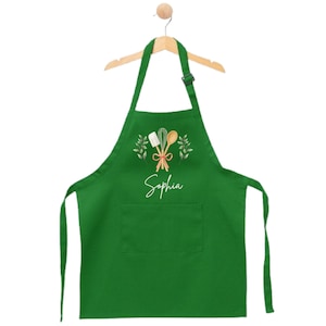 May include: Green kitchen apron with a pocket, featuring a white design of kitchen utensils and the name "Sophia" in white script.