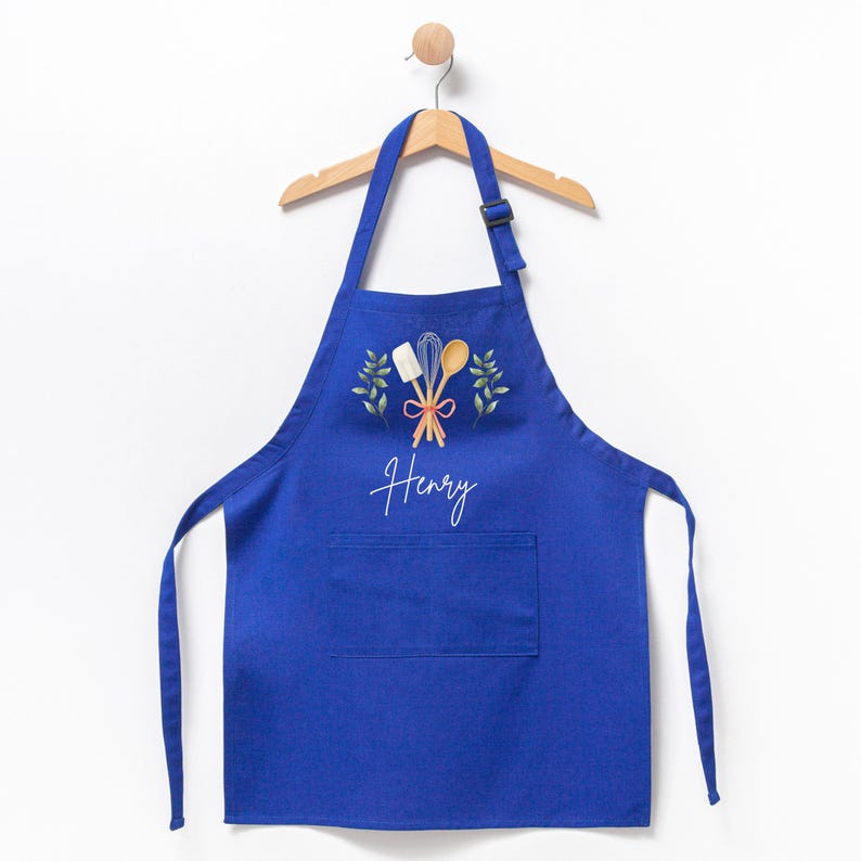 May include: A blue kitchen apron with a pocket, featuring a white design of kitchen utensils and greenery, with the name "Henry" written in white script.
