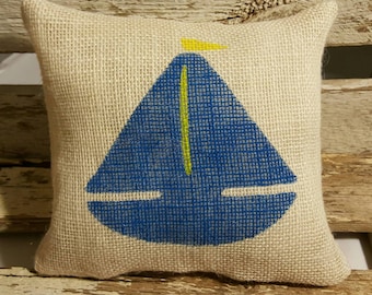 May include: A burlap pillow with a blue sailboat design. The sailboat has a yellow sail and a yellow mast.