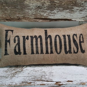 May include: A brown burlap pillow with the word "Farmhouse" printed in black.