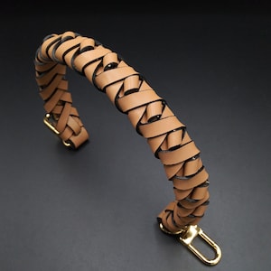 Könnte beinhalten: Ein brauner Ledergriff mit geflochtenem Design. Der Griff hat einen goldenen Haken aus Metall am Ende.