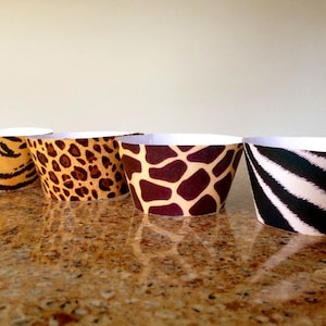 May include: Four cupcake cases featuring various animal print designs: tiger, leopard, giraffe, and zebra. The cases are white with brown, black, and yellow patterns.