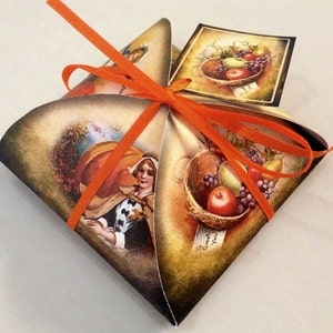 May include: A decorative gift box with a vintage illustration of a woman, a pumpkin, and a basket of fruit. The box is tied with an orange ribbon. A small tag with a fruit basket illustration is attached.